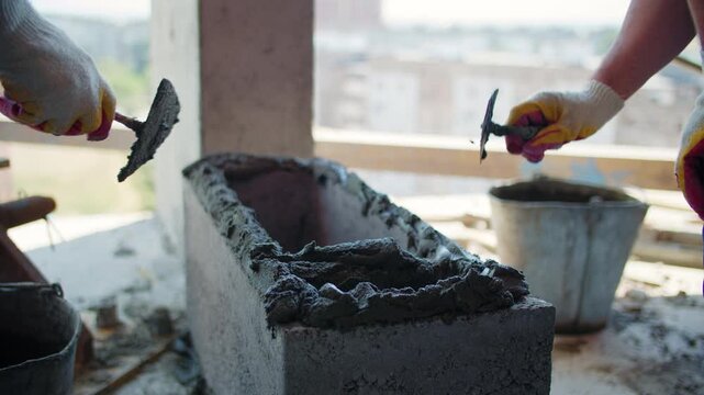 Construction workers spreading mortar on hollow concrete block