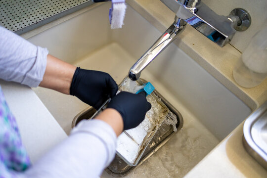 Dental Technician Cleaning Instrument Tray at Sink with Gloves