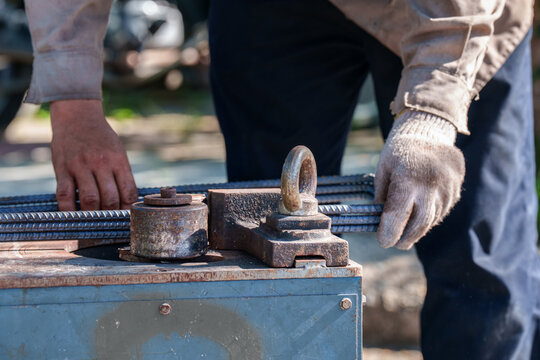 Close up of worker hands bending steel rebar with manual bending machine tool at construction site. Industrial work concept.
