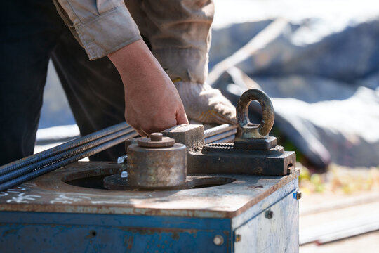 Close up of worker hands bending steel rebar with manual bending machine tool at construction site. Industrial work concept.
