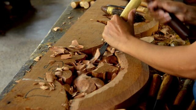 Closeup of a woodcarvers hands using a chisel and mallet to carve an intricate design into a wooden board