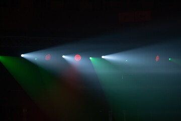 Fototapeta premium Stage spotlights pierce smoky air, colored beams sweep across empty stage, dramatic concert and theater lighting mood.
