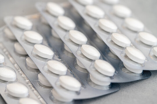 Multiple blisters of white round pills or tablets on a grey surface. Concept of medical treatment, pharmaceutical industry, and healthcare. Close-up of medicine packaging for pain relief, vitamins, 