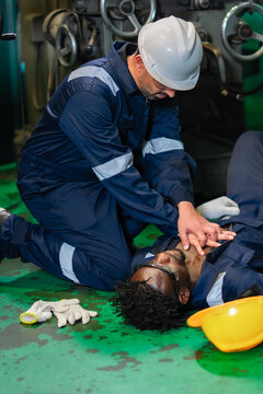 Industrial safety incident simulation showing trained worker providing CPR assistance to unconscious colleague inside manufacturing plant. Emergency preparedness, workplace rescue.