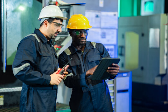 Skilled factory workers analyzing operational data on tablet computer beside industrial machinery. Engineering teamwork, predictive maintenance, process optimization, and smart manufacturing workflow.