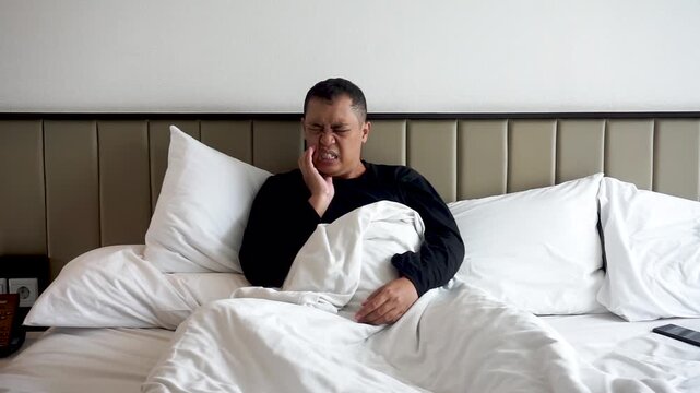 Asian man wearing black shirt show toothache expression at bed room. Feel pain on his teeth