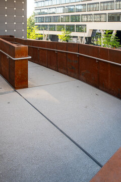Courtyard terrace in urban architecture shows a concrete pathway beside a rusted railing, where building facade, exterior, windows and light guide depth