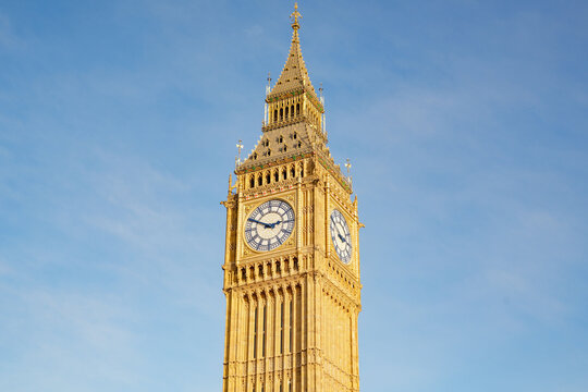 Big Ben clock tower illuminated by golden sunlight against blue sky in London, England