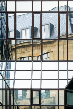 Through a glass grid, an older building appears inside modern architecture as windows, facade, reflections, contrast and urban exterior align