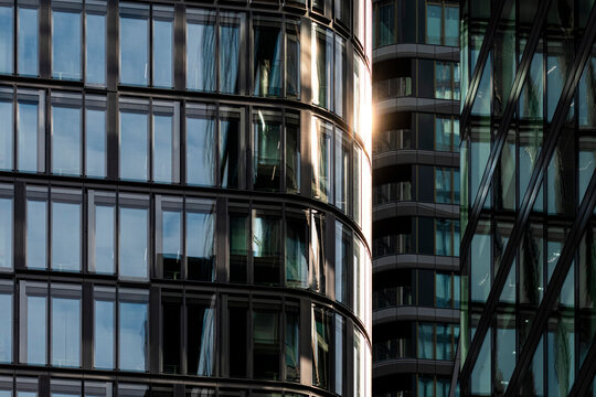 Between curved glass tower facades, sunlight sharpens modern skyscraper architecture as reflections, windows and office exterior overlap