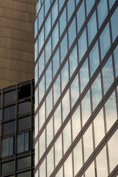 Across a glass facade, sky reflections and grid windows turn a modern skyscraper into urban architecture with office tower vertical lines