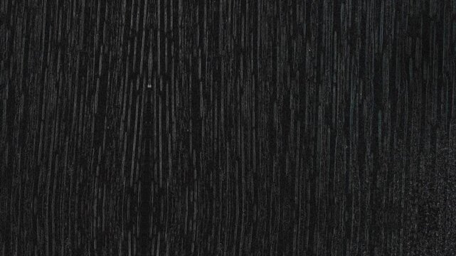 Dark textured surface with vertical streaks, resembling black wood grain or brushed material finish. Grunge texture background animation.