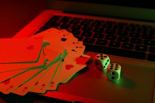 Laptop with playing cards and dices on table in casino, closeup