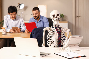 Human skeleton with telephone at table against male colleagues working in office