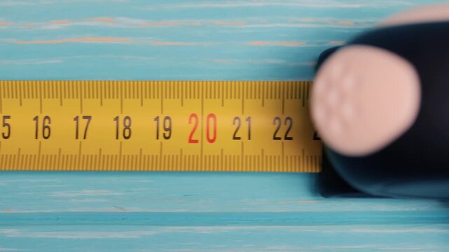 Yellow construction measuring tape extending over light blue wooden background in closeup motion sequence.