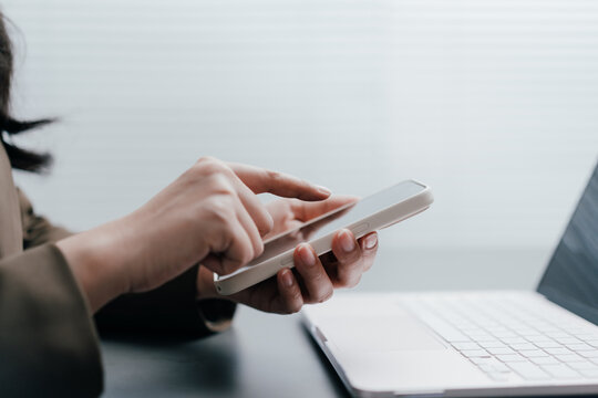 businesswoman touching a smartphone screen working with laptop. Professional female worker using mobile technology for digital banking, seacrching data, texting and online business
