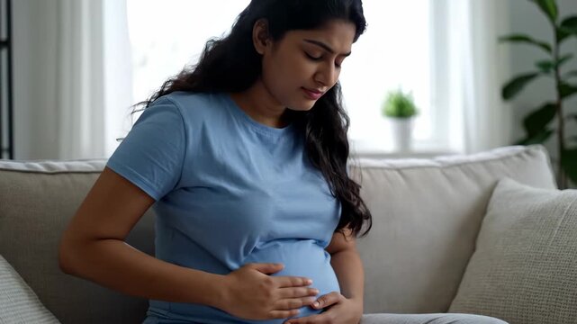 The scene of a pregnant woman caressing her belly on the sofa at home, when a pregnant woman caresses her belly warmly