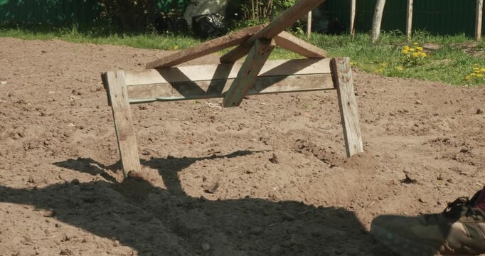 Male farmer using a handmade wooden marker to create furrows in the cultivated soil, meticulously preparing the vegetable garden bed for planting seedlings during a sunny spring day.