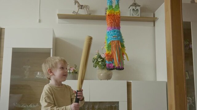 Young boy making his first hits on a festive birthday pi&ntilde;ata and realizing it is hard to break