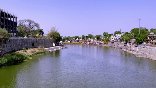 Handheld shot from Narasingh Ghat Bridge overlooking Shri Ram Ghat and the sacred Kshipra River in Ujjain. Temple ghats, riverfront architecture, and pilgrimage surroundings visible during daylight.
