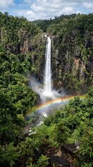 Fototapeta premium Majestic Waterfall Cascading Down Rocky Cliff with Rainbow in Lush Green Forest