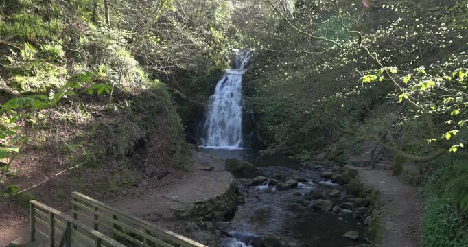revealing shot of the Gleno Waterfall with wooden bridge crossing a small stream