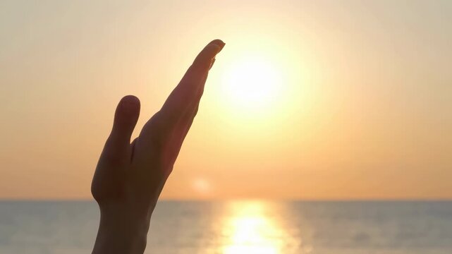 Silhouetted hand reaching toward a glowing sunset above a calm ocean