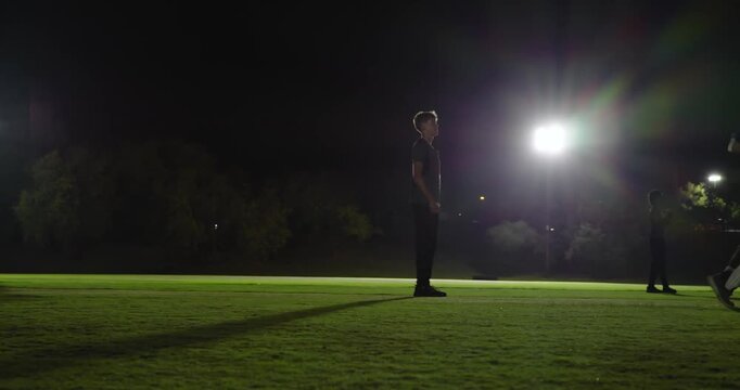 Diverse cricket players, floodlights, bowler running up delivering ball past stumps
