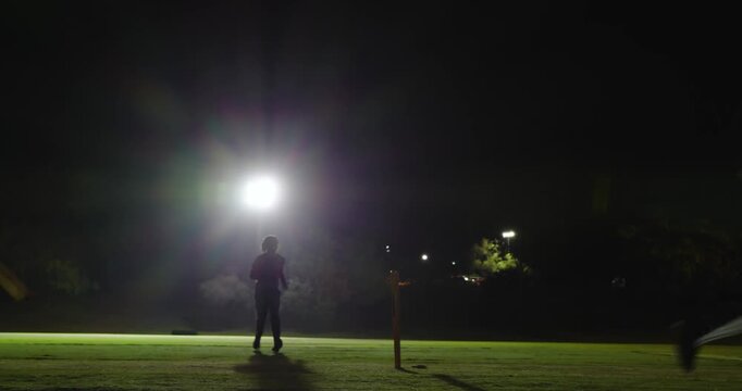 Diverse teammates following bowler starting runup, keeper catching ball celebrating, floodlit night