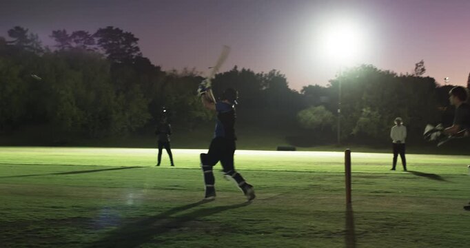 Teenage boy batsman taking bowler delivery on dusk pitch driving ball into outfield and running