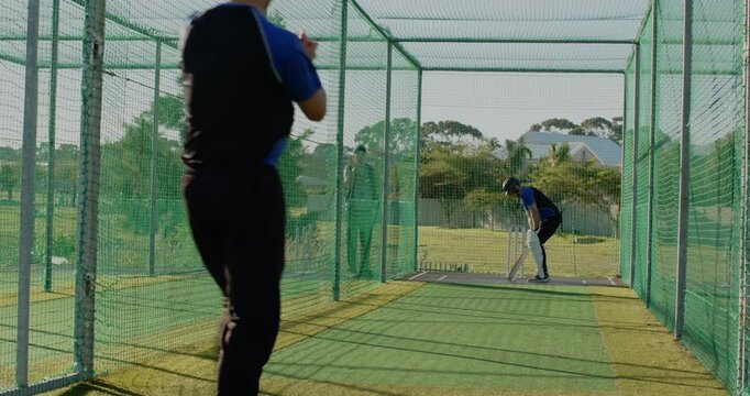 Practicing male coach with player inside cricket net cage, with cricket bat and pads, copy space