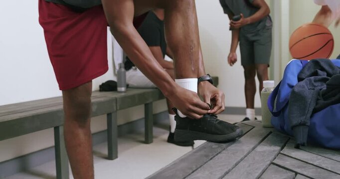 Gesturing friends sparking african american man tying shoelaces for practice in locker room