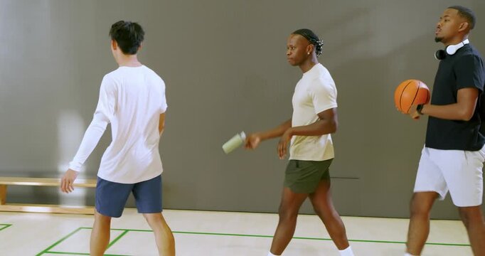 Teammate walking triggers diverse male friends jogging, dribbling ball at wooden bench for game