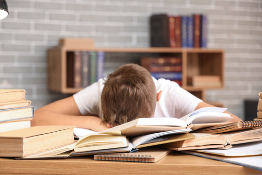 Tired teenage boy with books at table in library