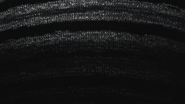 macro pan of black textured knit fabric catching moody cinematic light across curved abstract weave patterns