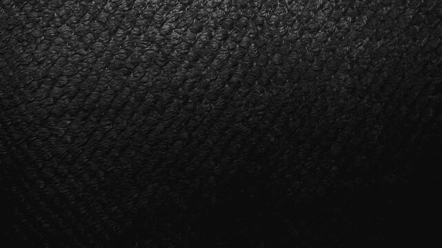 cinematic macro pan shifts light across dark black textured knit fabric revealing intricate organic loop patterns