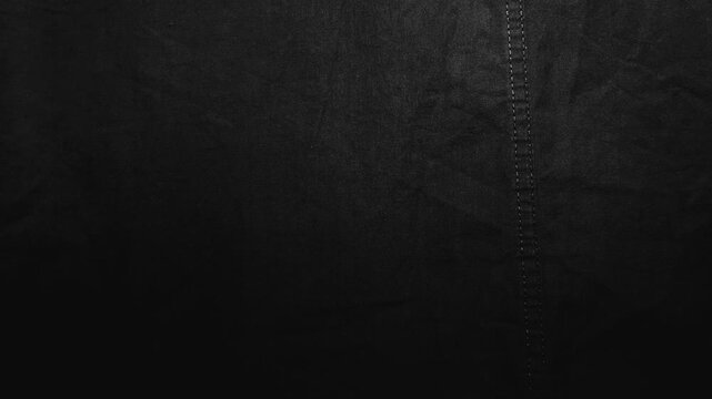 cinematic macro camera pans across textured black linen fabric with subtle double stitching revealing detailed weave
