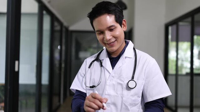 Young Asian male doctor or nurse in blue scrubs using a digital tablet and stylus pen in a modern clinic.