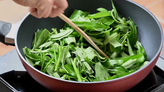 Stir-frying morning glory with minced garlic and chili in a hot pan, popular Thai street food
