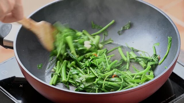 Stir-frying morning glory with minced garlic and chili in a hot pan, popular Thai street food