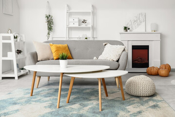 Obraz premium Interior of light living room with electric fireplace, pumpkins and sofa