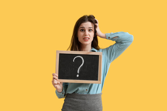 Stressed female teacher holding chalkboard with question mark on yellow background