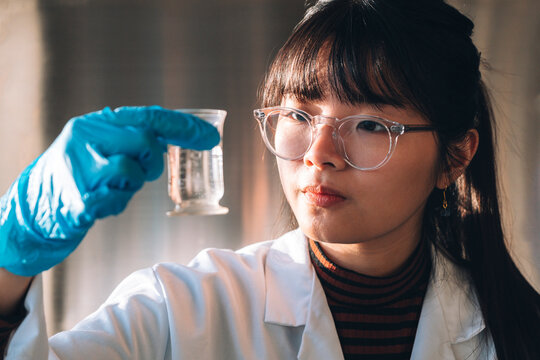 Young scientist wearing eyeglasses examining solution in glassware