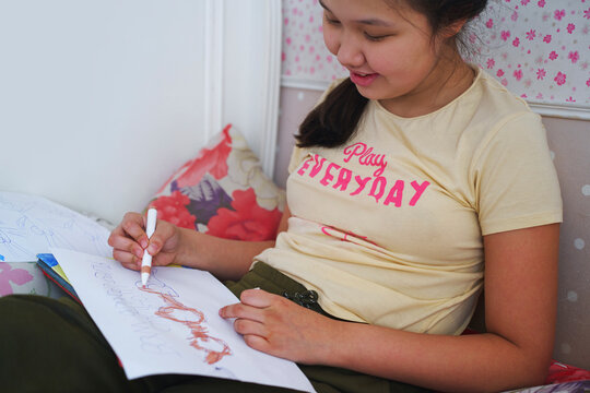 Smiling student drawing on paper while relaxing on a bed at home