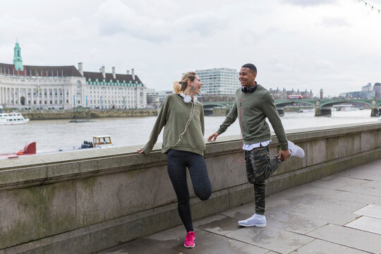 UK, London, two happy runners stretching at riverwalk