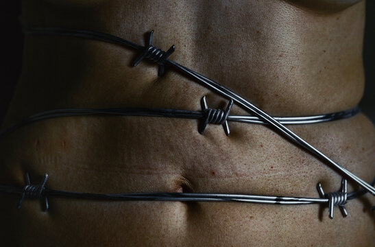Bare abdomen tightly wrapped in sharp barbed wire indoors