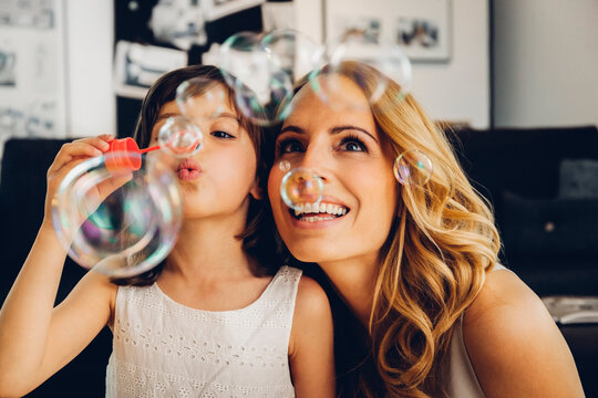 Happy mother with daughter at home blowing soap bubbles