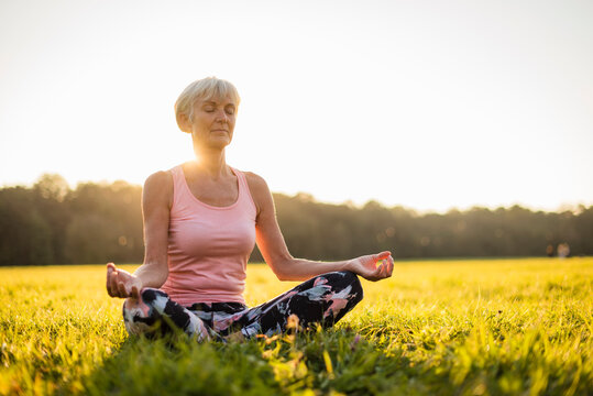 Senior woman in lotus position on rural meadow at sunset