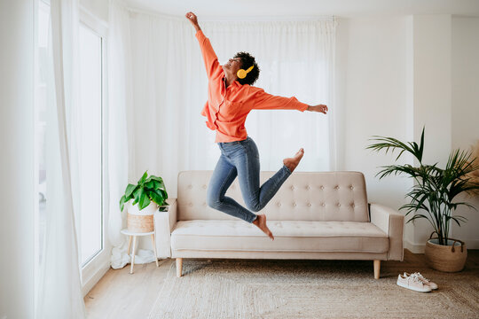 Carefree freelancer wearing wireless headphones jumping at home office