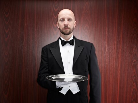 Professional butler presenting an empty silver tray indoors